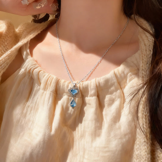 This exquisite sterling silver necklace captivates with its vintage and elegant design. The pendant features a beautifully carved heart motif, centered with a charming light blue gemstone. Below the heart, a teardrop-shaped pendant, also set with a blue gemstone, dangles gracefully. The overall design exudes classical charm and refined craftsmanship. The necklace comes with a classic silver chain, designed to grace the wearer's neck with nobility and taste.