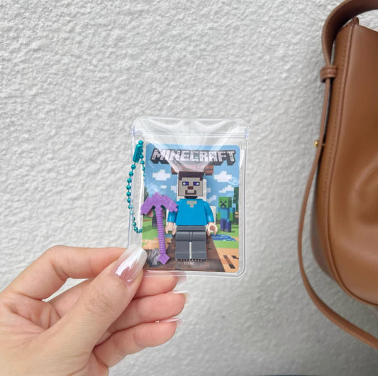 Minecraft Skeleton Steve Keychain. Features Steve in skeleton form with a purple pickaxe, encased in a clear pouch with a beaded chain for backpacks.