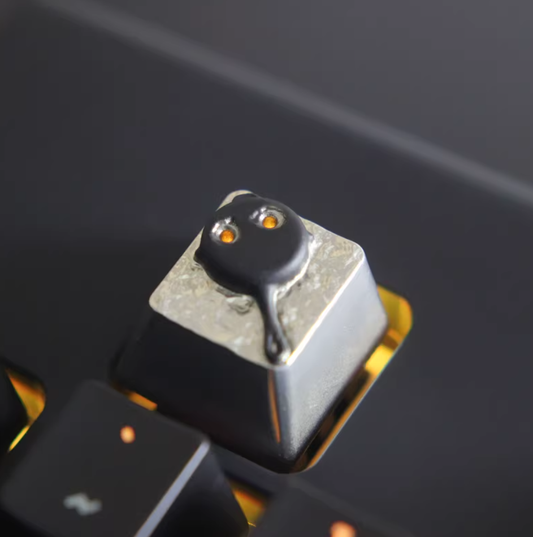 PUBG frying pan metal keycap, 3D melting effect, silver base, black pan, orange eyes, installed on mechanical keyboard, close-up.