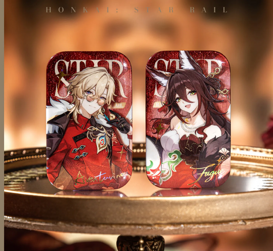 Two rectangular glittery badges from Honkai: Star Rail are placed on a golden tray. On the left is Aventurine (red background, red formal attire), and on the right is Fugue (red background, elegant dress with fox ears). The background is a warm, textured orange-brown.
