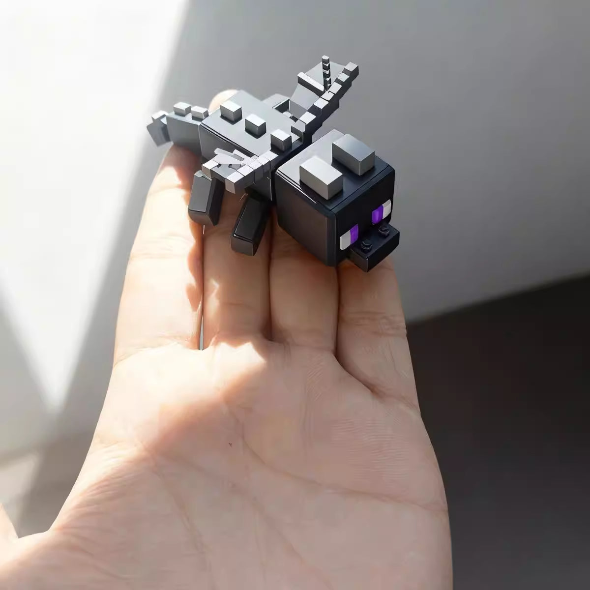 Small black and gray pixel-style dragon figurine with purple eyes resting on a person’s hand in natural light.If you want it more SEO-focused (e.g. for a product page) or more lifestyle-focused, I can refine it further.