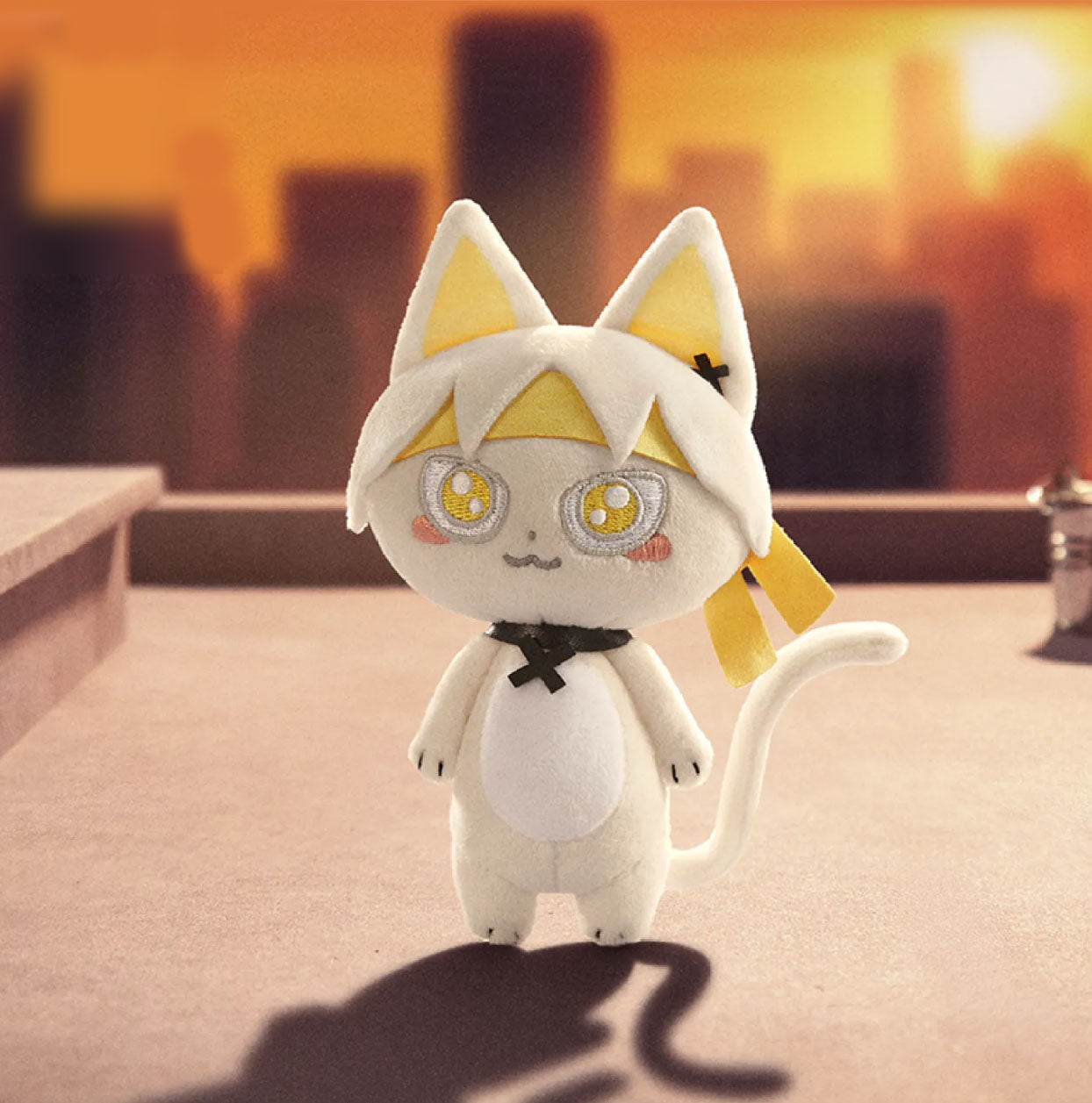 This is a white cat doll. It has pinkish-yellow inner ears and yellow accents on its head, with large, round eyes that have yellow and white embroidered details and pink blush marks on its cheeks. 