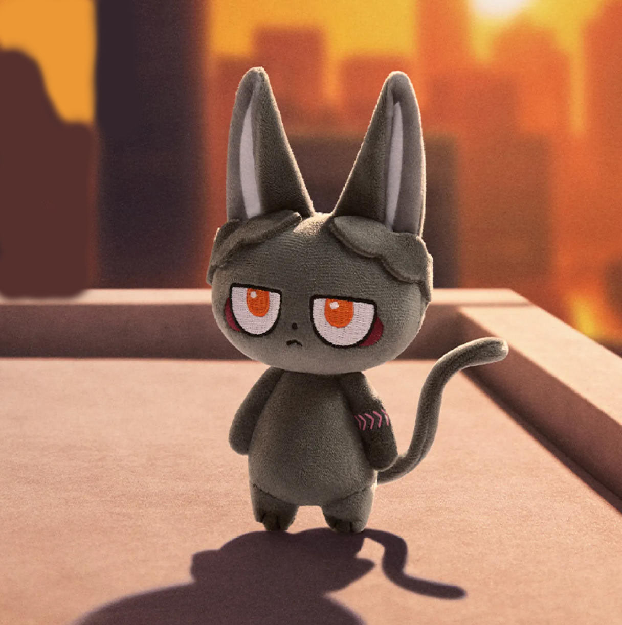 This is a dark gray cat doll. It has long, pointed ears with white inner linings, large orange eyes with white and red details, and a slight frown expression. 