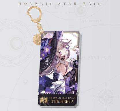 This Honkai: Star Rail acrylic keychain features The Herta in a glamorous witch outfit, with a golden clasp and chain, set against a soft pink and white background.