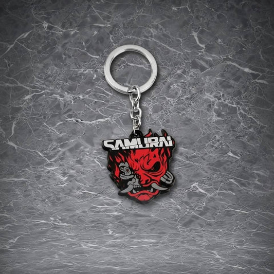 This is a keychain featuring a fierce, red and black samurai - inspired demon - like face with the word "SAMURAI" prominently displayed on it, attached to a metal ring via a chain.