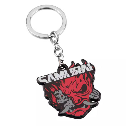 This is a keychain featuring a fierce, red and black samurai - inspired demon - like face with the word "SAMURAI" prominently displayed on it, attached to a metal ring via a chain.