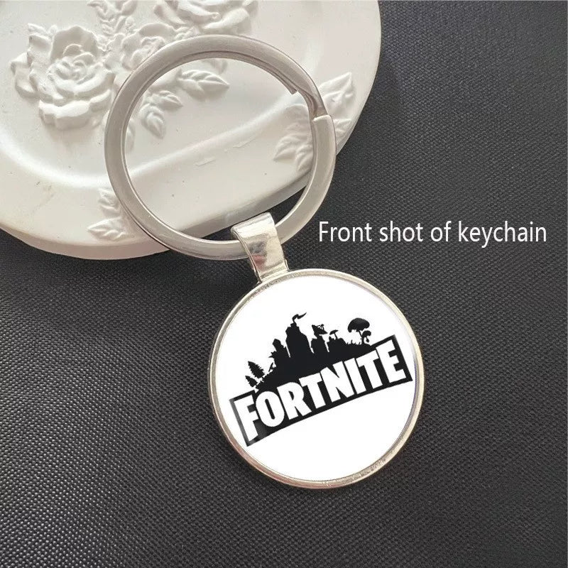 Round Fortnite-themed keychain featuring the game logo with battle royale skyline silhouette, set in a polished silver metal frame. The scratch-resistant pendant is lightweight, ideal for attaching to keys, backpacks, or bags. A sleek collectible for fans.