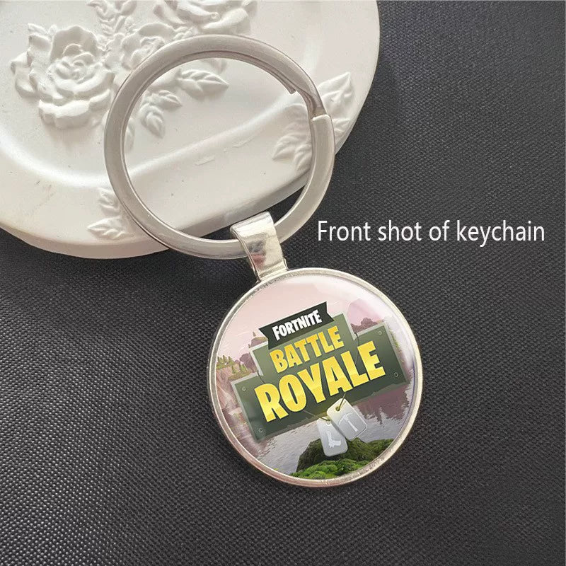 Round Fortnite Battle Royale keychain featuring the iconic game logo with vibrant battlefield artwork, set in a polished silver metal frame. It has a scratch-resistant glass dome cover and a sturdy split ring, perfect for attaching to keys, backpacks, or bags. A fun collectible for fans.