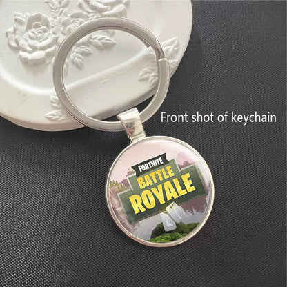 Round Fortnite Battle Royale keychain featuring the iconic game logo with vibrant battlefield artwork, set in a polished silver metal frame. It has a scratch-resistant glass dome cover and a sturdy split ring, perfect for attaching to keys, backpacks, or bags. A fun collectible for fans.