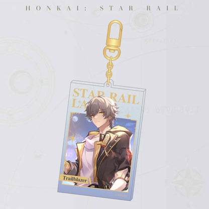 A single Honkai: Star Rail acrylic card keychain with a gold carabiner. It features the male Trailblazer, with “STAR RAIL LANE” in gold foil and the character’s name at the bottom.