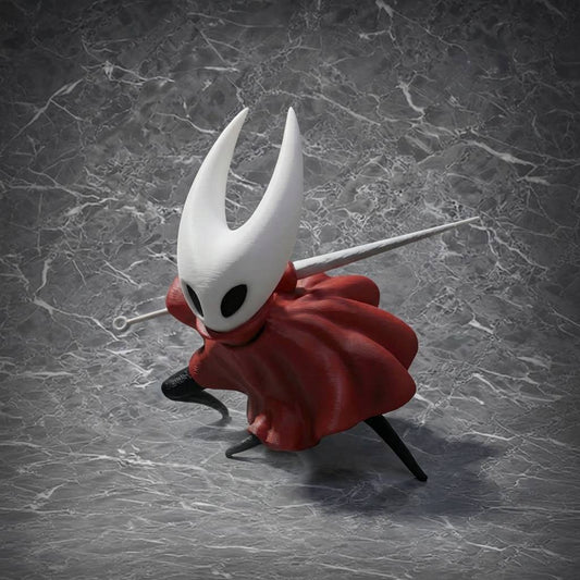 This is a detailed figurine of a character from the game "Hollow Knight," featuring a white horned mask, a flowing red cloak, and holding a unique weapon, surrounded by colorful flowers and creatures, perfect for collectors and fans of the game.