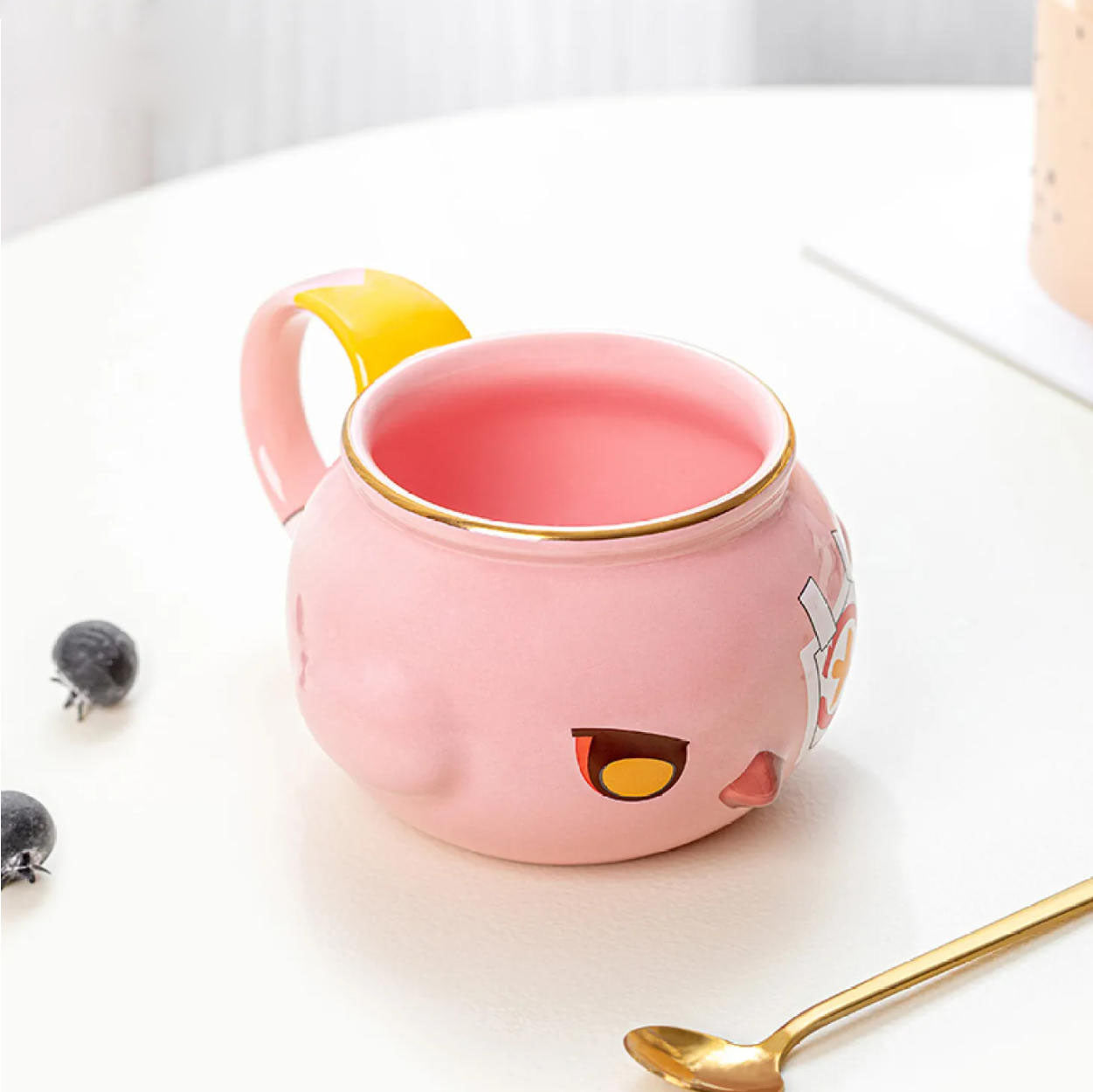 The mug sits on a white table with blueberries and a gold spoon, showcasing its practical use and charming design that adds a playful touch to your daily beverage routine.