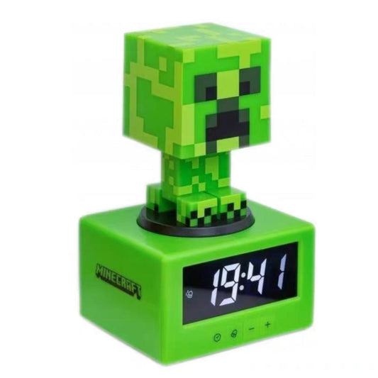 Minecraft Creeper Illuminated Alarm Clock, displayed against a soft pink background. The pixelated green design features a detachable Creeper figure atop a glowing digital clock base, with a height of approximately 16 cm, capturing the iconic blocky aesthetic of the game.