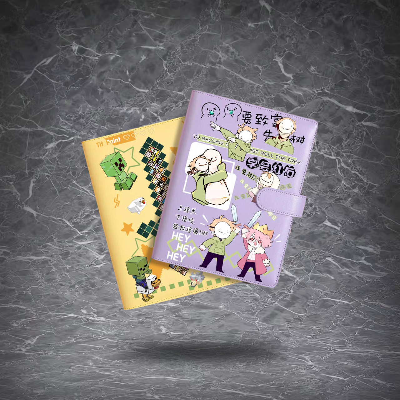 Two vibrant, game-themed journal notebooks are stacked against a dark marble background. One features a sunny yellow cover with pixelated green mob art, and the other a playful pink cover with meme-style characters and text. 