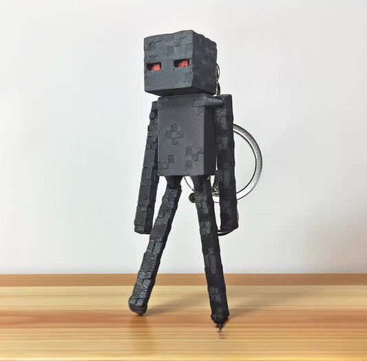 3D printed Enderman keychain from Minecraft, displayed against a soft pink background and wooden surface. The figure features fully articulated limbs