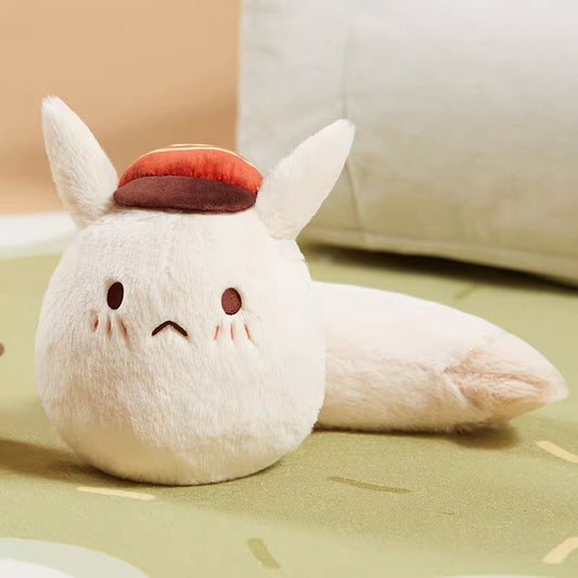 It wears a small hat with a red top and brown brim. The toy has simple facial features: two dark eyes, a small downturned mouth, and blushing cheeks. Its long, soft tail extends behind it.