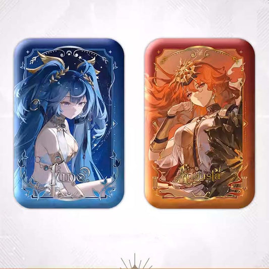 A side-by-side display of two rectangular tinplate badges: June’s blue celestial design and Augusta’s warm orange sunlit design, both with foil accents.
