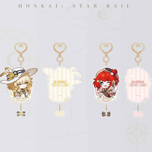 This image showcases two chibi-style acrylic keychains from Honkai: Star Rail. On the left is Aglaea, a blonde girl in a white hat with a gold rose, and on the right is Tribbie, a red-haired girl holding a drink. Both have heart-shaped clasps and small bow pendants.