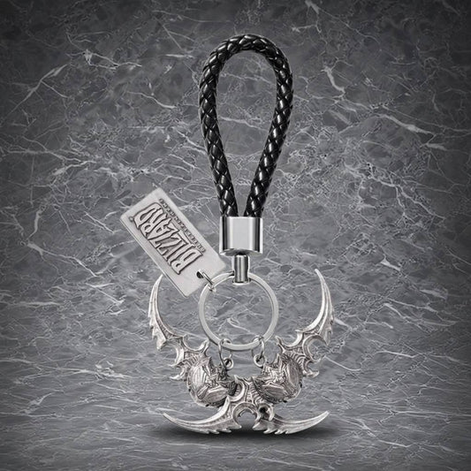 This is a sleek, Blizzard Entertainment-themed keychain featuring a detailed, silver-colored, twin-bladed weapon charm with intricate designs, attached to a black braided leather loop, perfect for gamers and collectors.