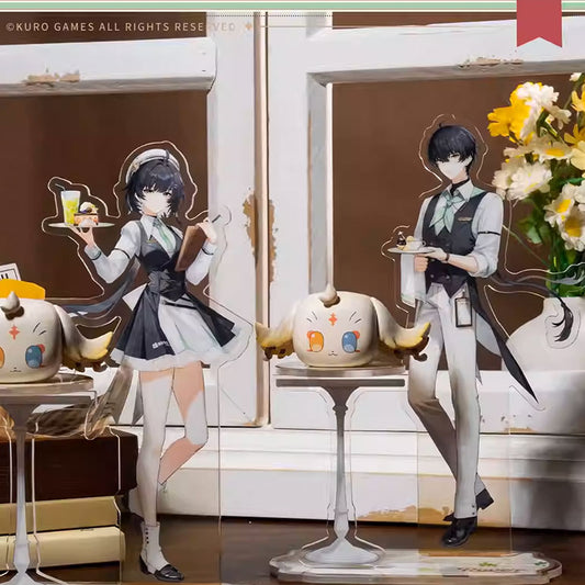 Two Wuthering Waves acrylic stands of the Male and Female Wanderers in cafe uniforms, paired with Puff companions, displayed in a cozy cafe backdrop with tables and flowers.